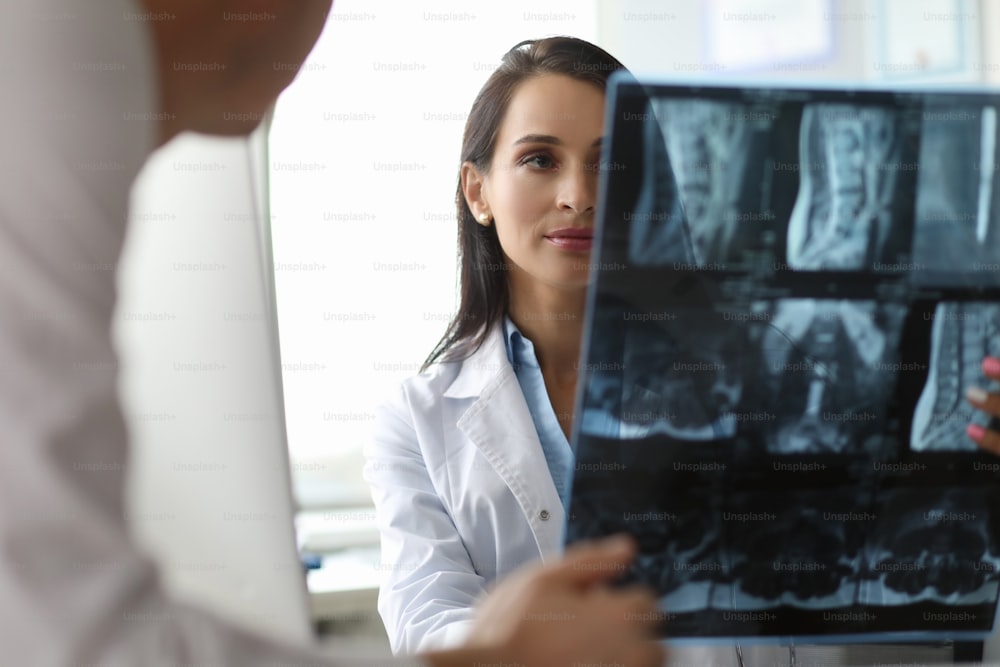 Portrait of serious surgeon looking carefully on spine x-ray in different projections. Cute doc discussing disease diagnosis with colleague. Healthcare concept