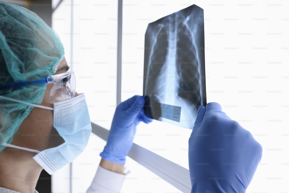 Una doctora con máscara médica protectora y gafas mira una imagen de rayos X. Concepto de examen médico de órganos internos