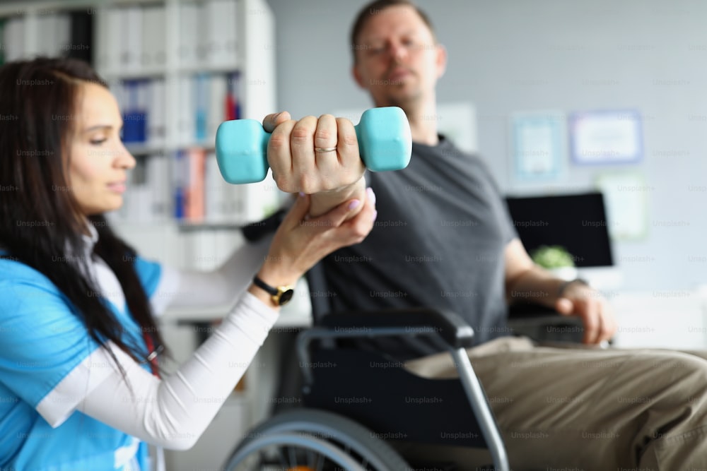 Rehabilitation therapist helping disabled man in wheelchair to lifting dumbbell in closeup. Rehabilitation of patients after trauma concept