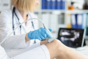 整形外科医は、オフィスで患者の膝の超音波検査を行います。診療所で足の骨と関節の超音波検査を受けている若い女性