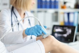 Orthopedic doctor makes ultrasound examination of patient knee in office. Young woman undergoing ultrasound of bones and joints of legs in clinic