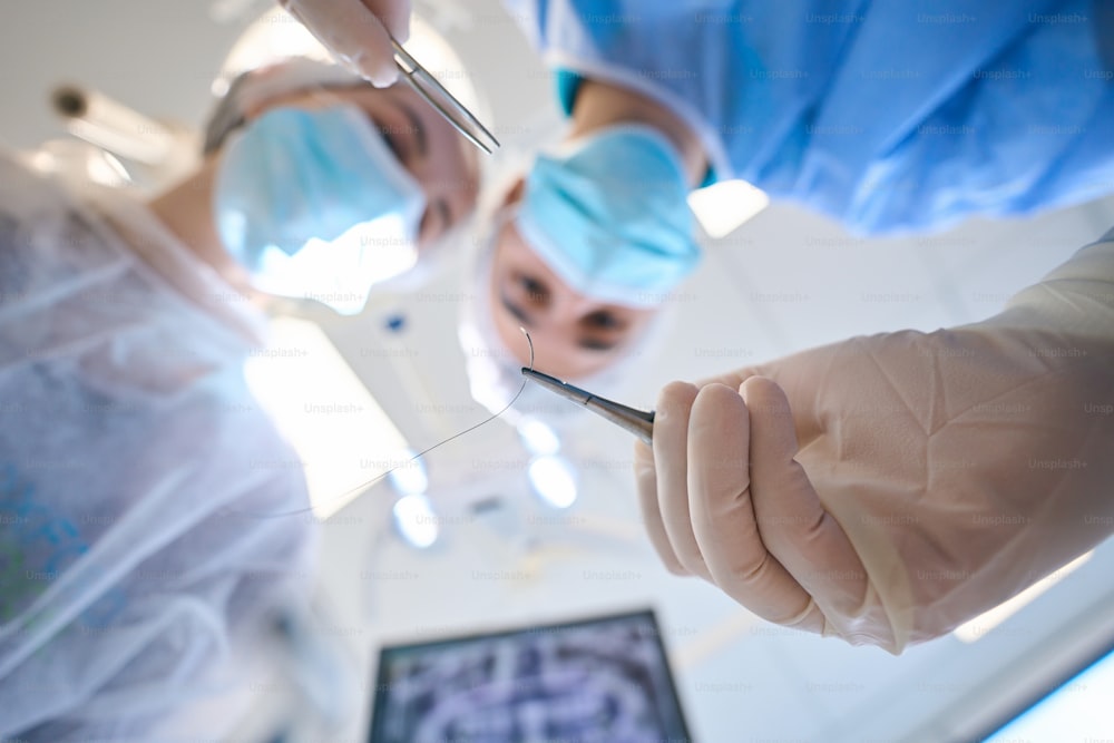 Joven cirujano sostiene una aguja quirúrgica especial en sus manos, una asistente femenina está cerca