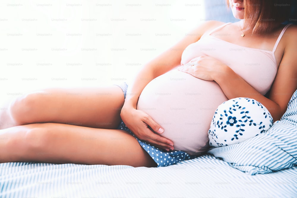 아름다운 임산부가 집의 침실에서 배에 손을 잡고 있습니다. 아기를 기다리는 젊은 엄마. 임신, 출산, 건강 관리, 산부인과, 의학의 개념. 클로즈업, 실내.