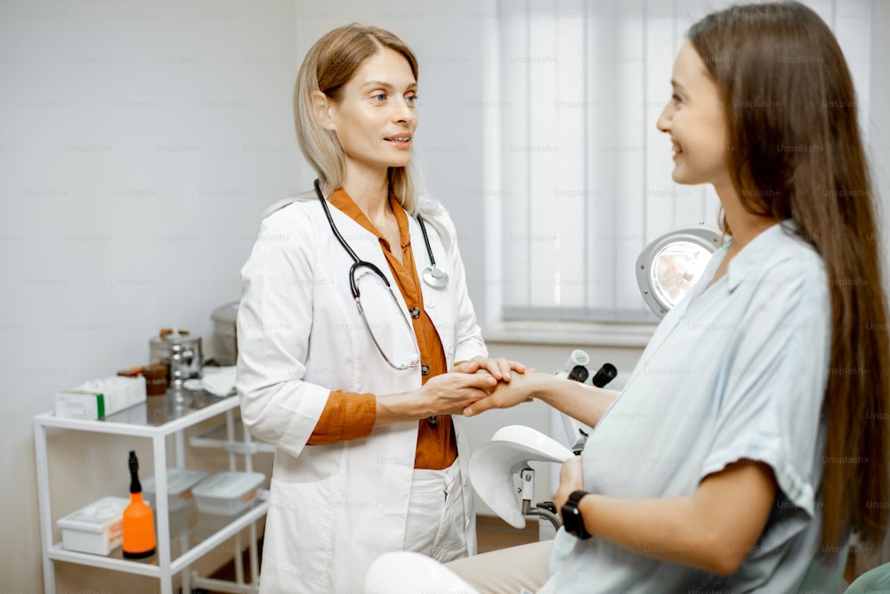 Young pregnant woman sitting on the gynecological chair during a medical consultation with gynecologist. Cheerful doctor supporting and comforting patient