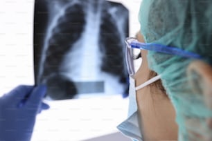 Un médico con mascarilla protectora y guantes está mirando una radiografía. Examen médico de la neumonía en el concepto de coronovirus