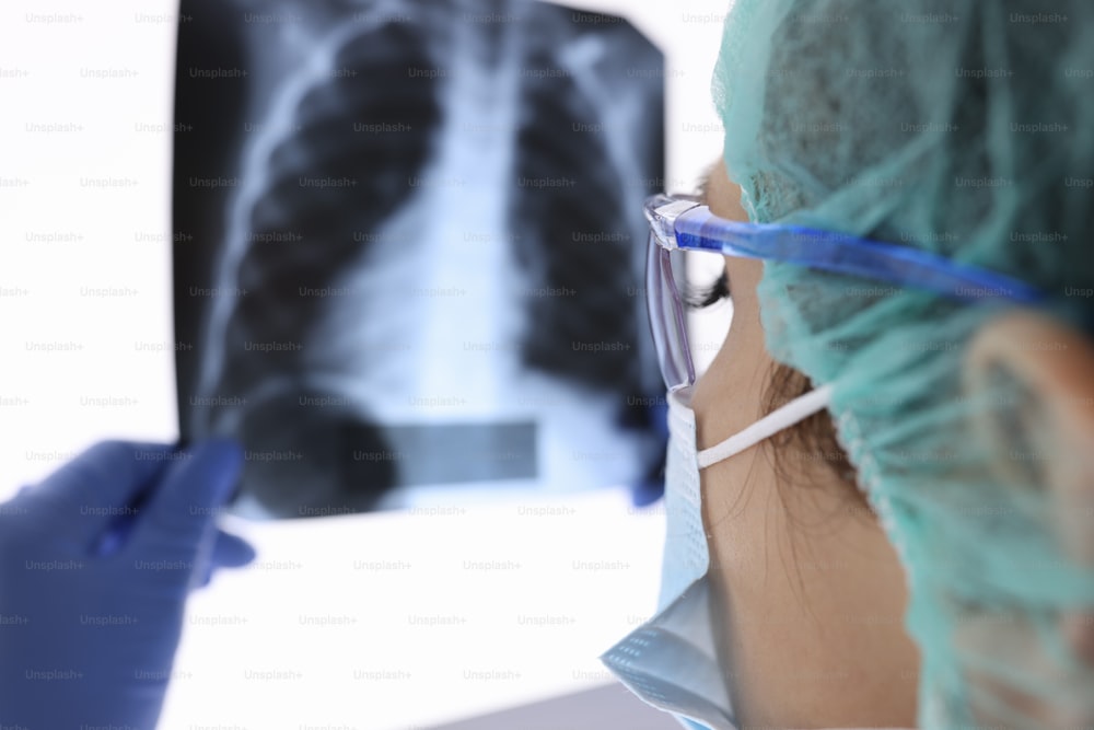 Doctor with protective medical mask and gloves is looking at an X-ray. Medical examination of pneumonia in coronovirus concept