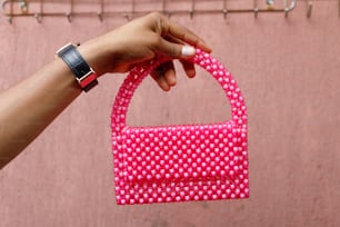 a hand holding a pink purse in front of a pink wall