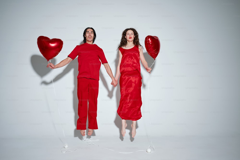 a man and a woman holding red heart shaped balloons