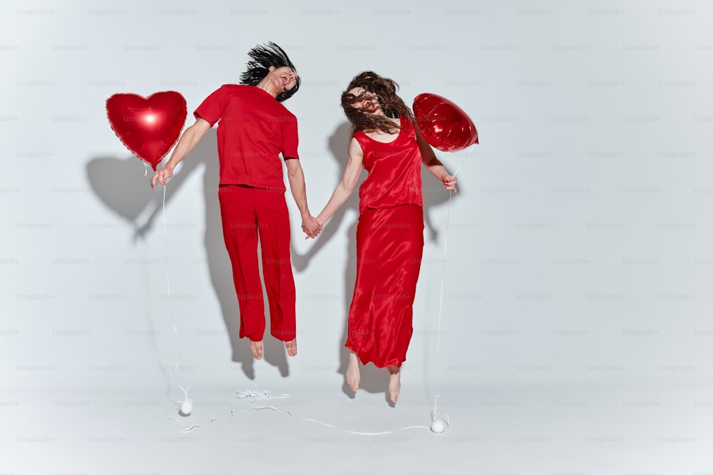 a man and a woman holding hands while holding red heart balloons