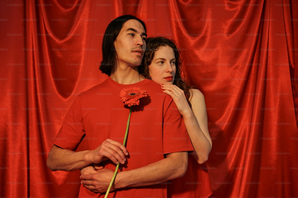 a man standing next to a woman in front of a red curtain