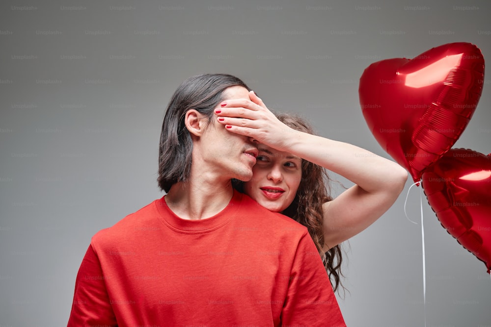 a woman covering her eyes next to a man holding a heart shaped balloon