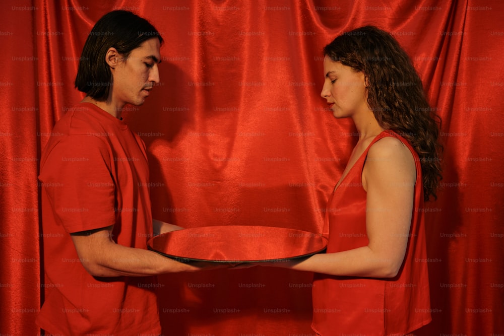 a man and a woman holding a plate in front of a red curtain