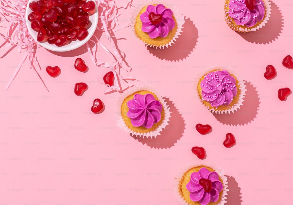 분홍색 배경에 보라색 설탕 프로스팅과 하트가 있는 컵케이크