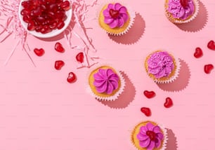 Cupcakes con glaseado morado y corazones sobre fondo rosa