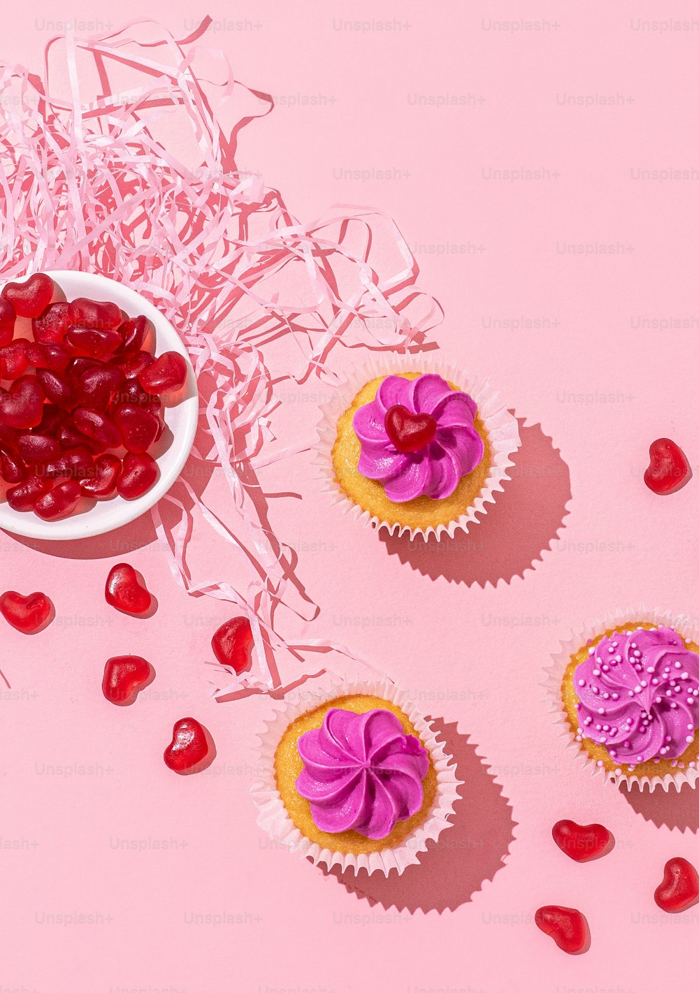 분홍색 프로스팅과 위에 리본을 얹은 컵케이크 3개