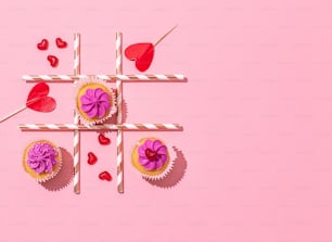 Cupcakes con glaseado rosa y corazones sobre fondo rosa
