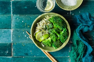 a bowl of broccoli and noodles with chopsticks