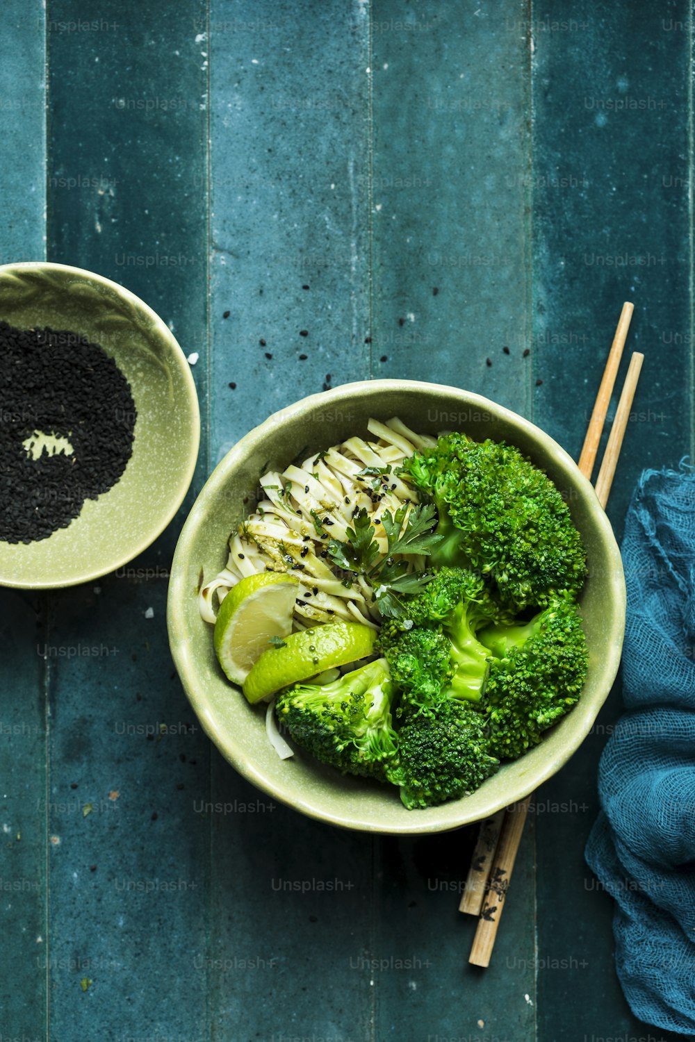 a bowl of broccoli and noodles with chopsticks