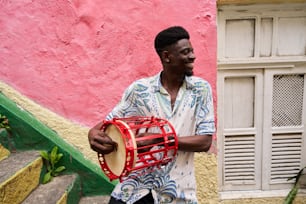 a man holding a drum in front of a pink wall