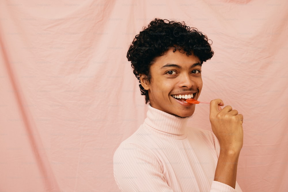 a woman brushing her teeth in front of a pink backdrop