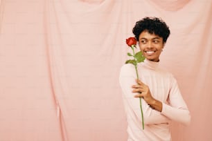 a woman holding a rose in front of a pink wall