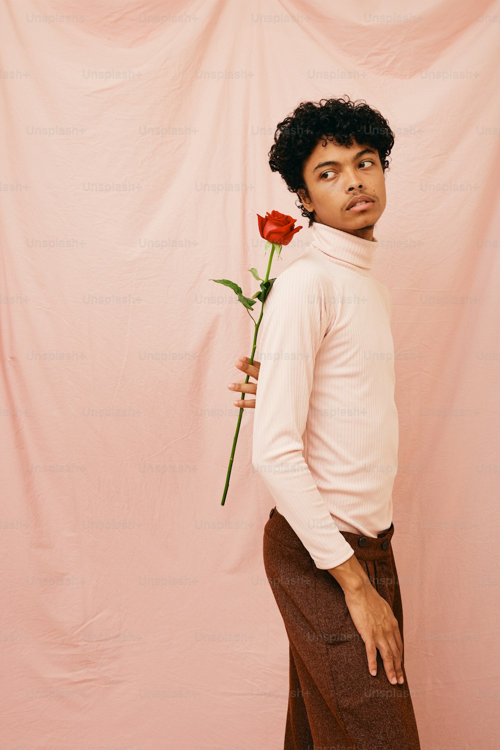 a man holding a rose in front of a pink background