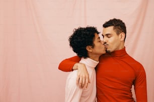 a man and woman kissing each other in front of a pink backdrop