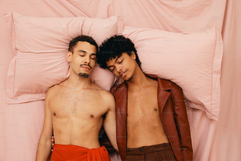 a couple of men laying next to each other on top of a bed