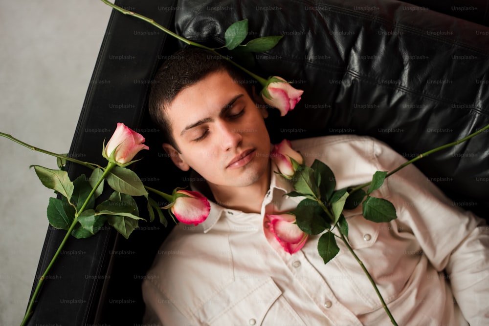 首にバラの花を巻いてソファに横たわる男性