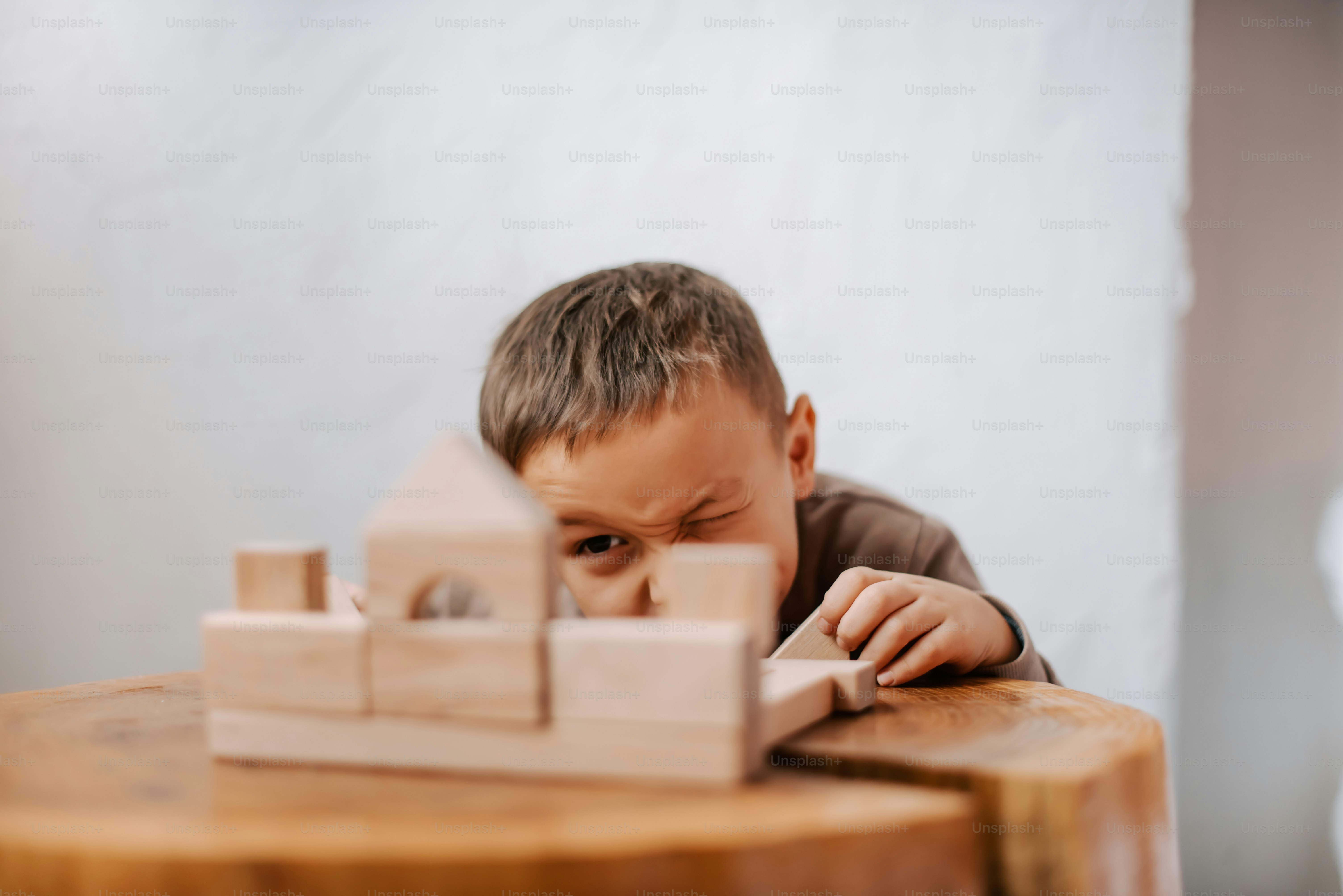 a young boy sitting at a table looking through a piece of wood