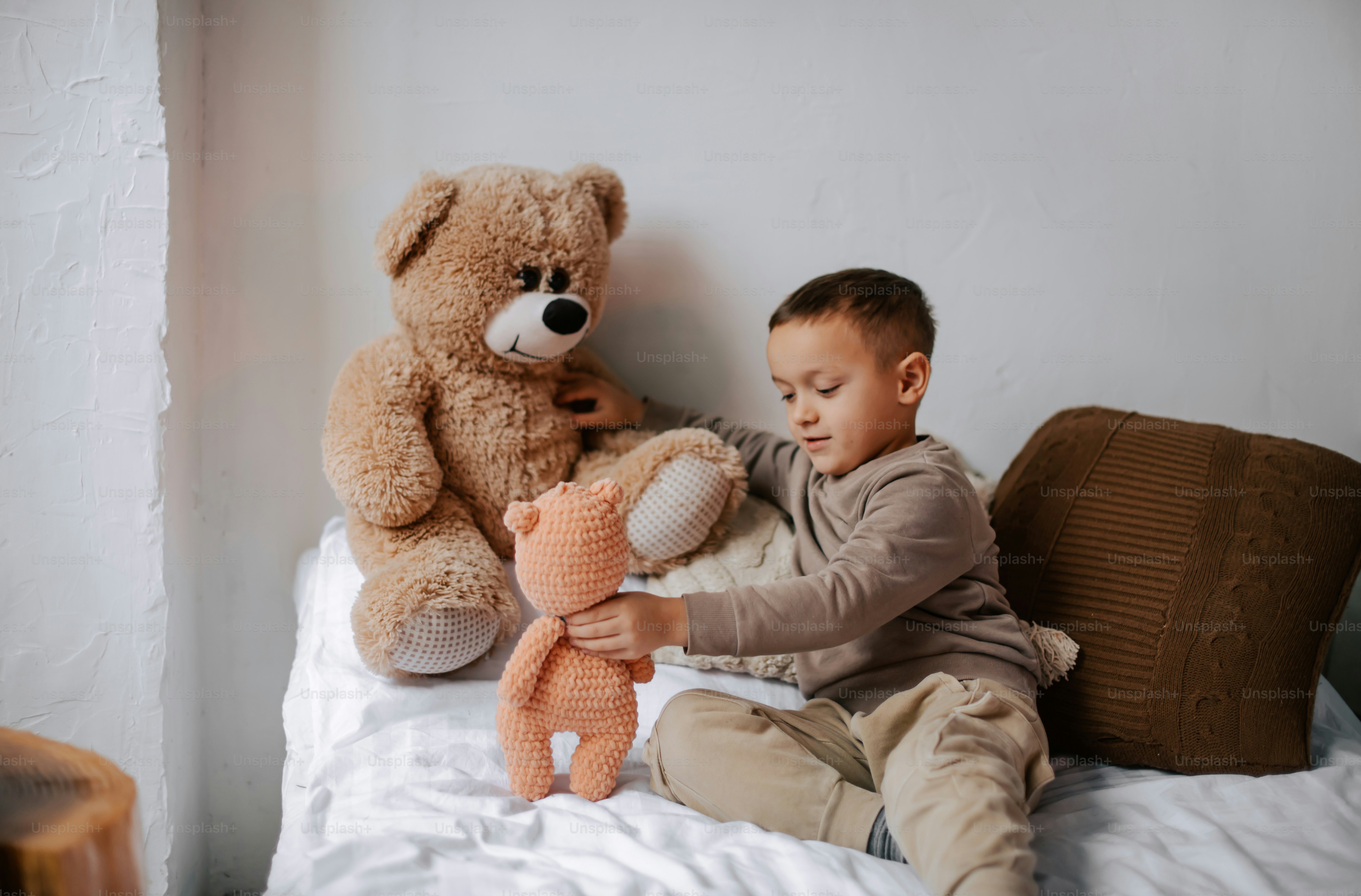 A little boy sitting on a bed with a teddy bear photo – Cuddly toys ...