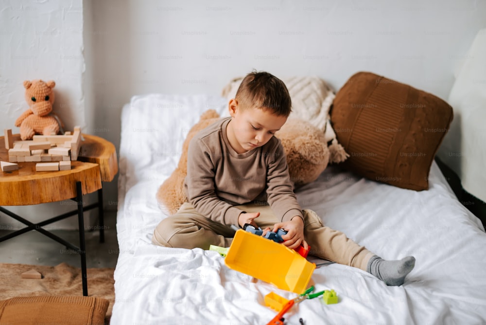 a little boy sitting on a bed playing with a toy