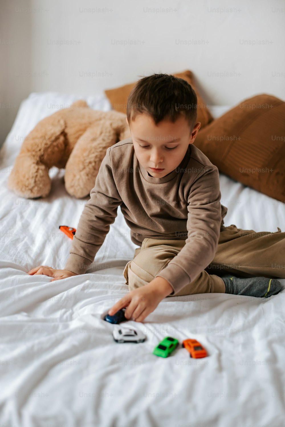 a young boy sitting on a bed playing with toys