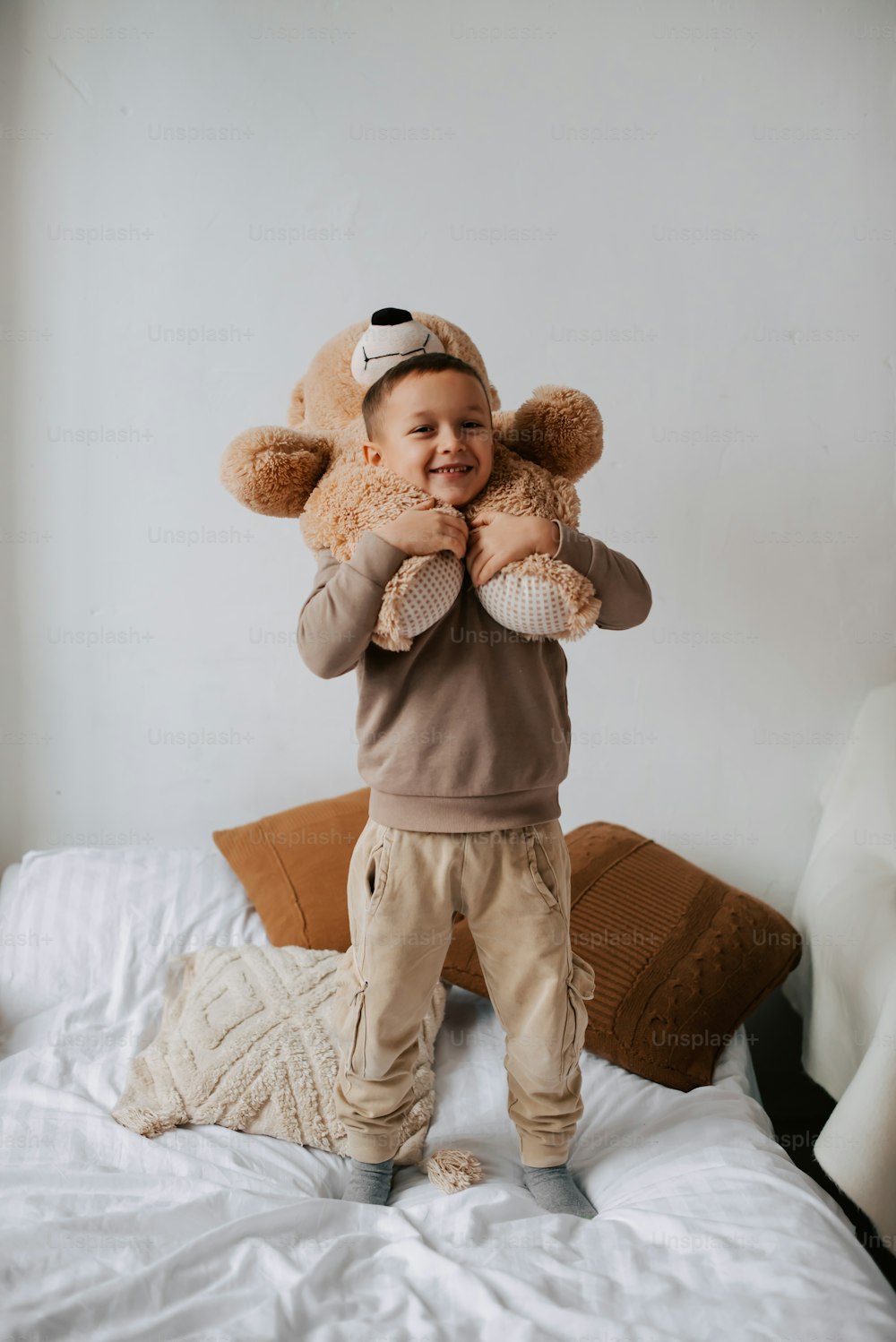 a little boy standing on top of a bed holding a teddy bear