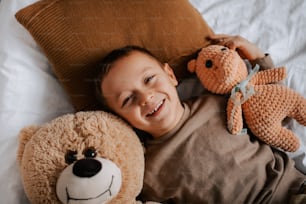 a little boy laying on a bed with two stuffed animals