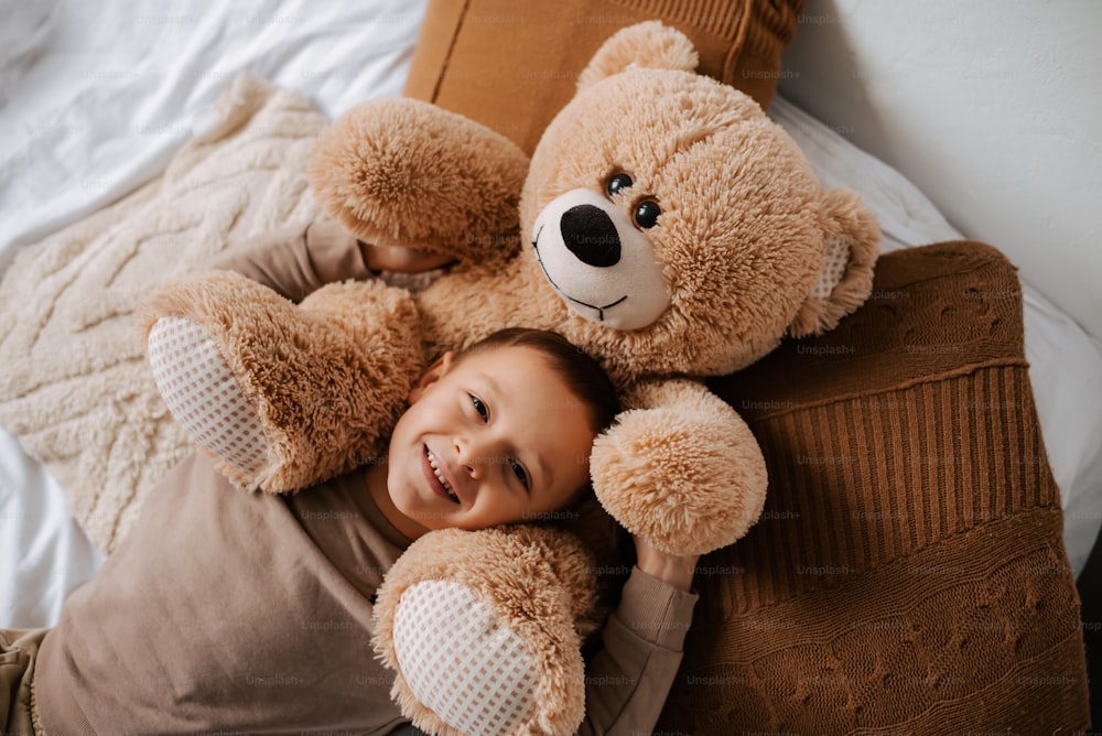 a little girl laying on a bed with a teddy bear