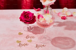 uma mesa rosa com duas taças de vinho e uma rosa