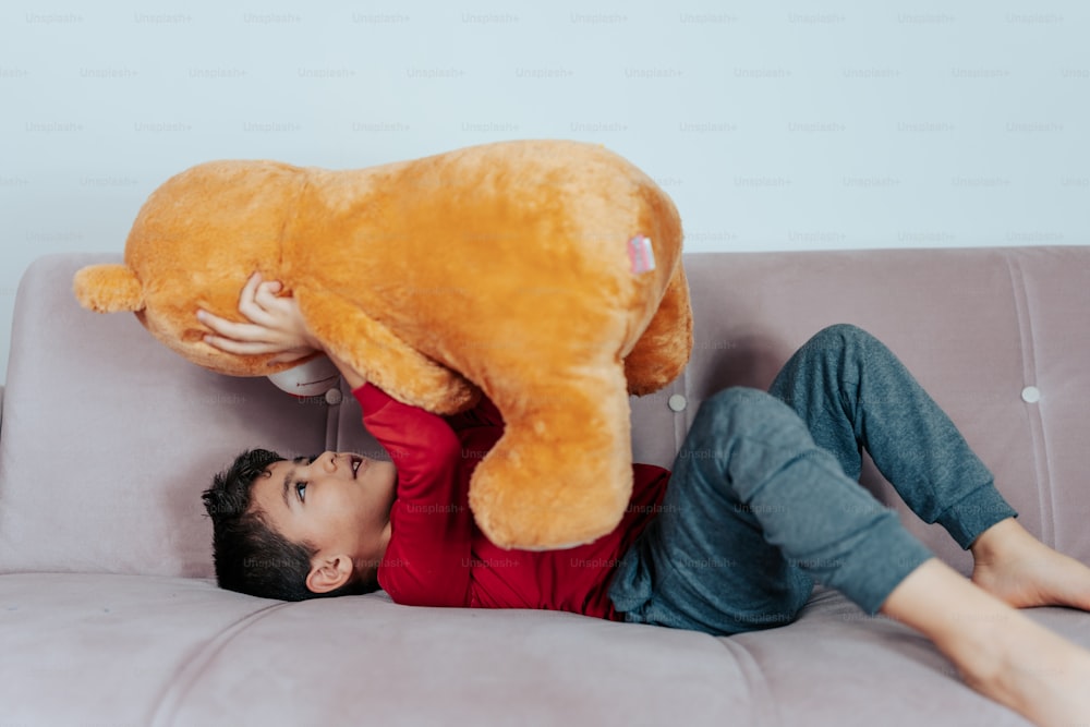 a boy laying on a couch with a large stuffed animal