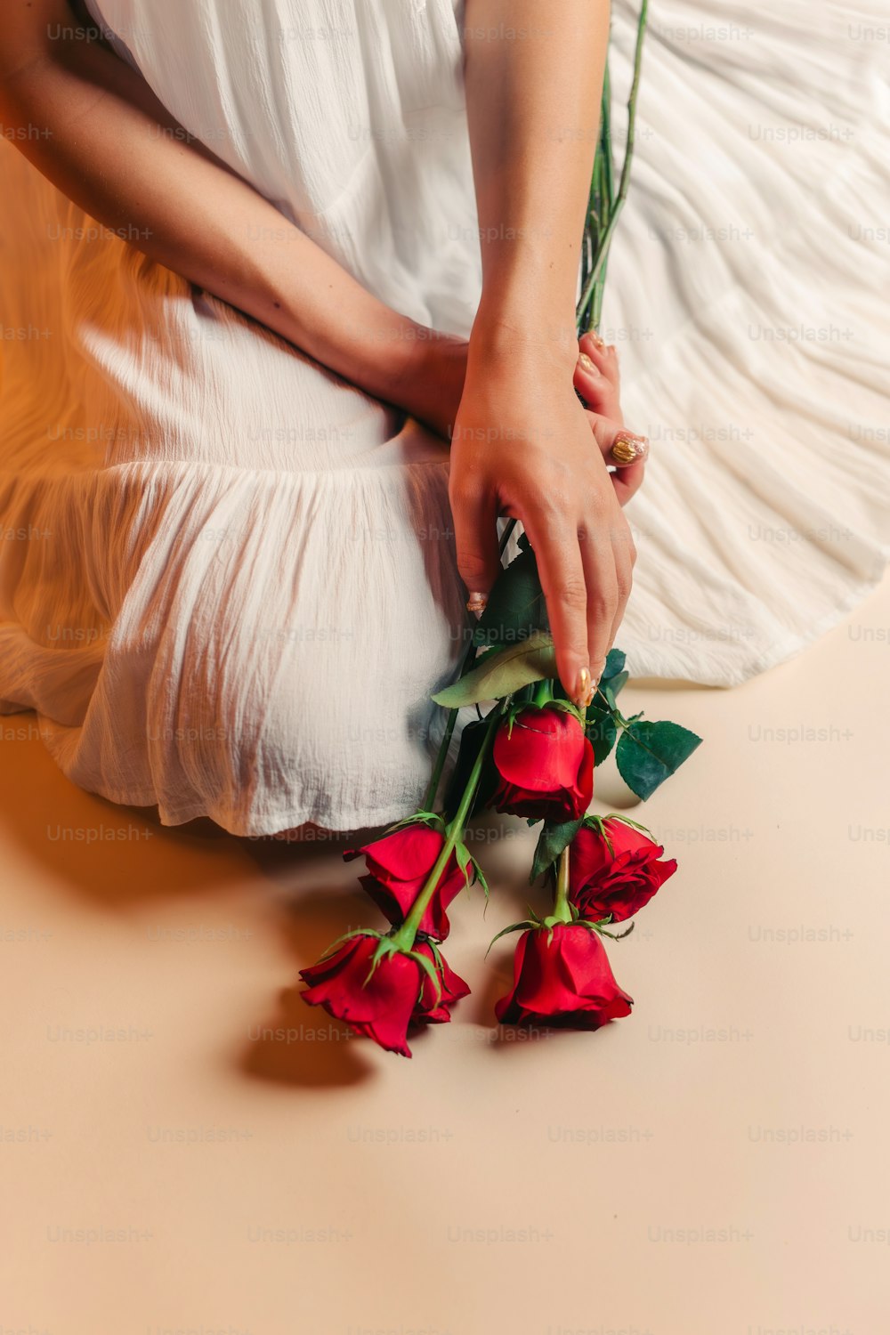 eine Frau in einem weißen Kleid mit einem Strauß roter Rosen in der Hand