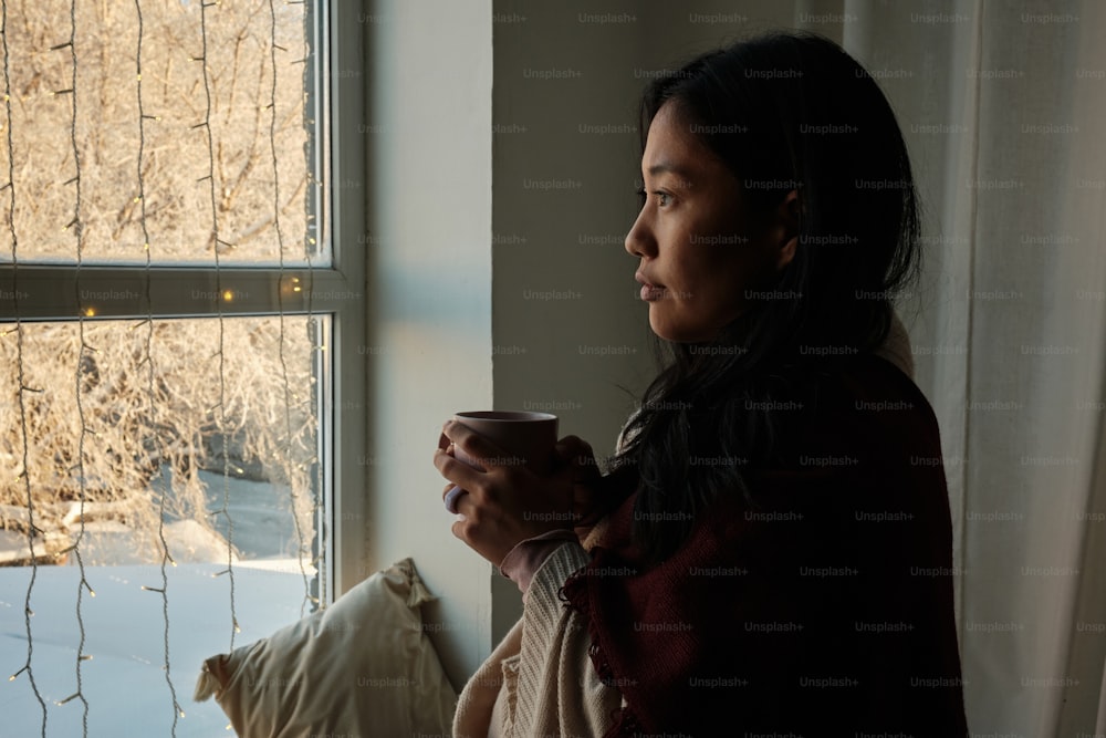 a woman holding a cup looking out a window