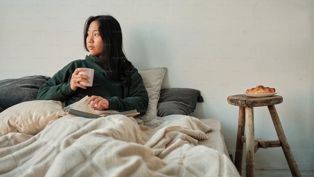 a woman sitting on a bed holding a cup of coffee