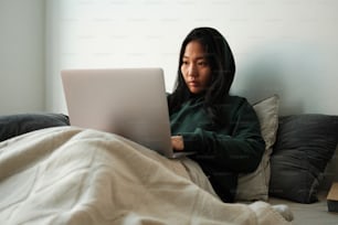 침대에 앉아 노트북 컴퓨터를 사용하는 여성