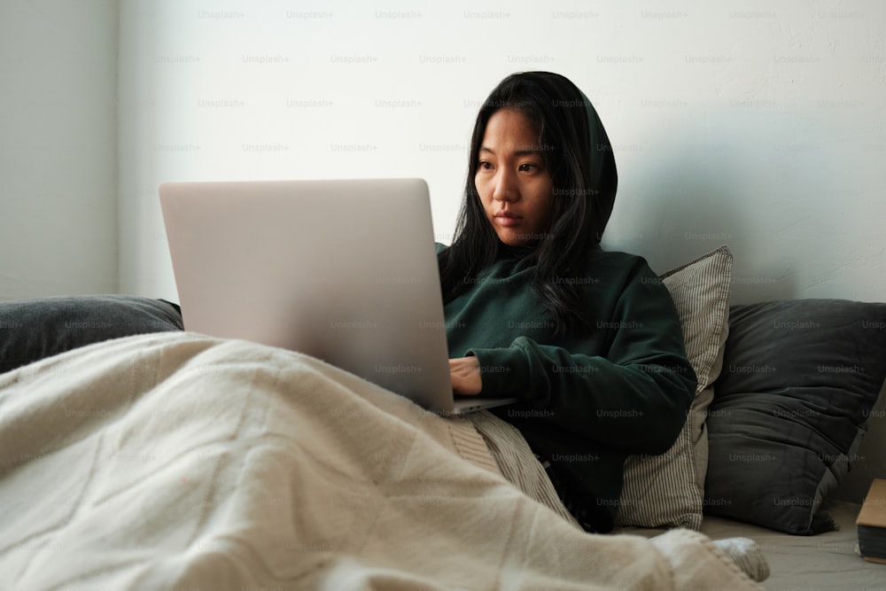 uma mulher sentada em uma cama usando um computador portátil