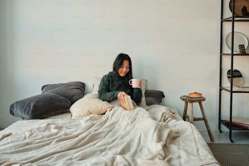 a woman sitting on a bed holding a cup of coffee