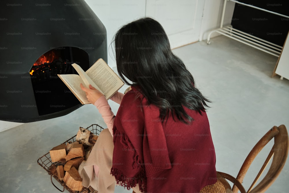 a woman reading a book in front of a fireplace