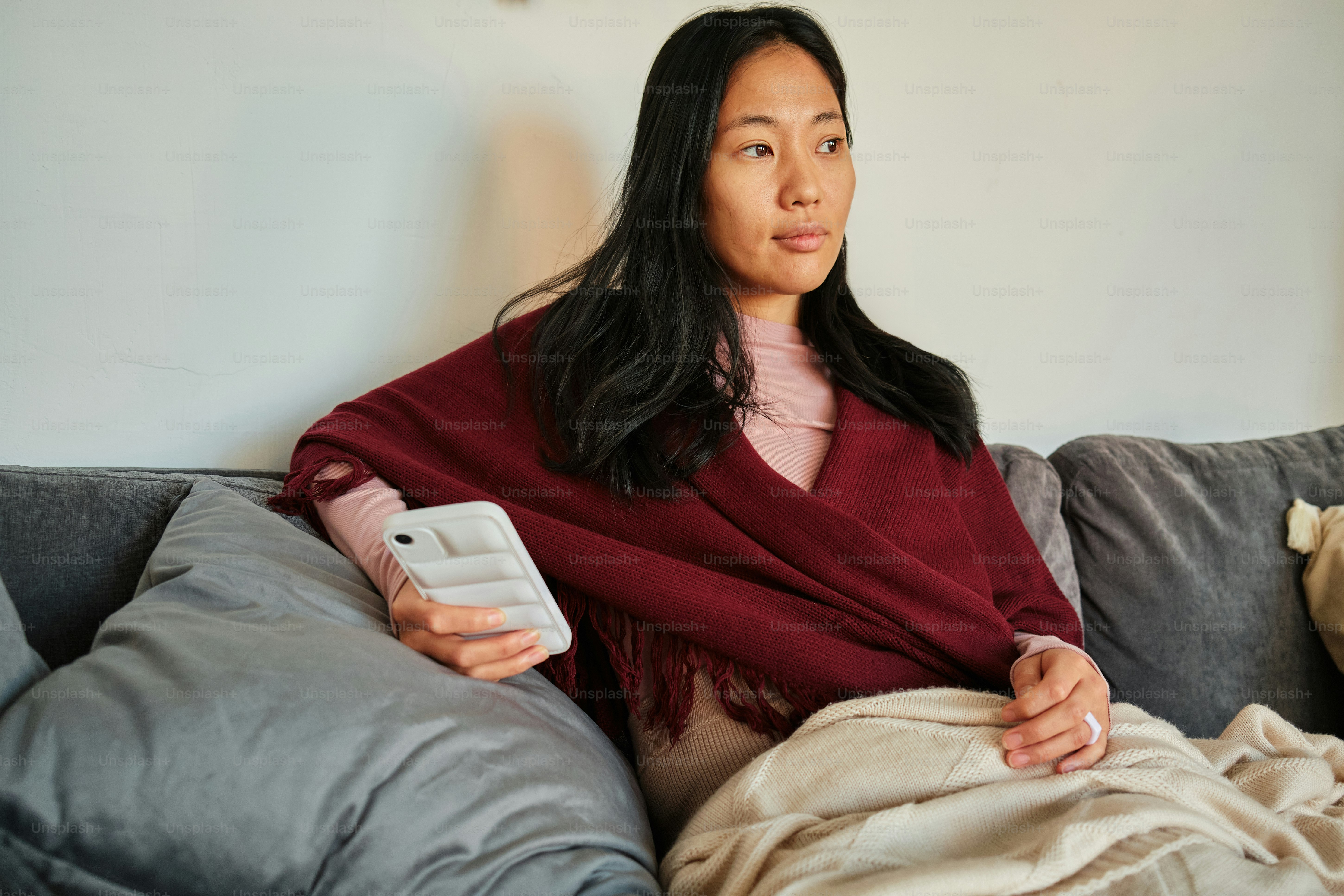 seorang wanita duduk di sofa sambil memegang ponsel