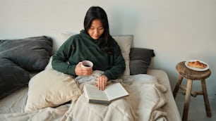 a woman sitting on a couch holding a cup of coffee and reading a book
