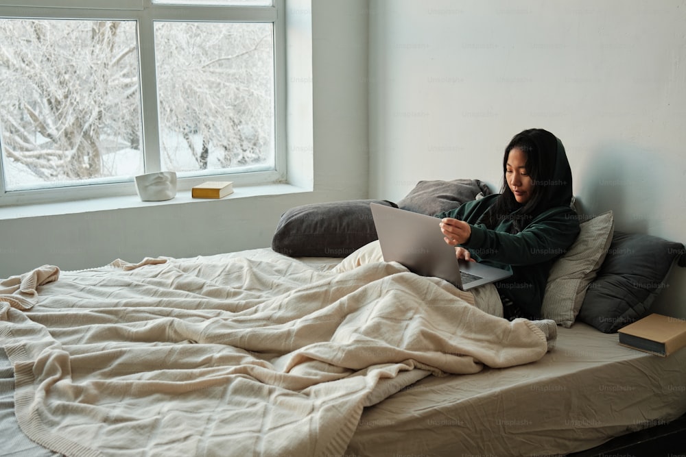 a woman sitting on a bed using a laptop computer