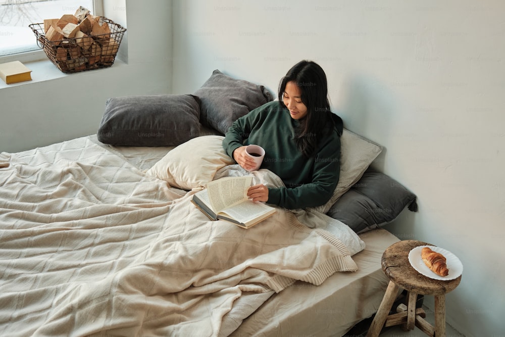 eine Frau sitzt auf einem Bett und liest ein Buch