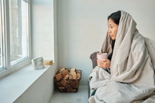 una donna seduta sul davanzale di una finestra con in mano una tazza di caffè